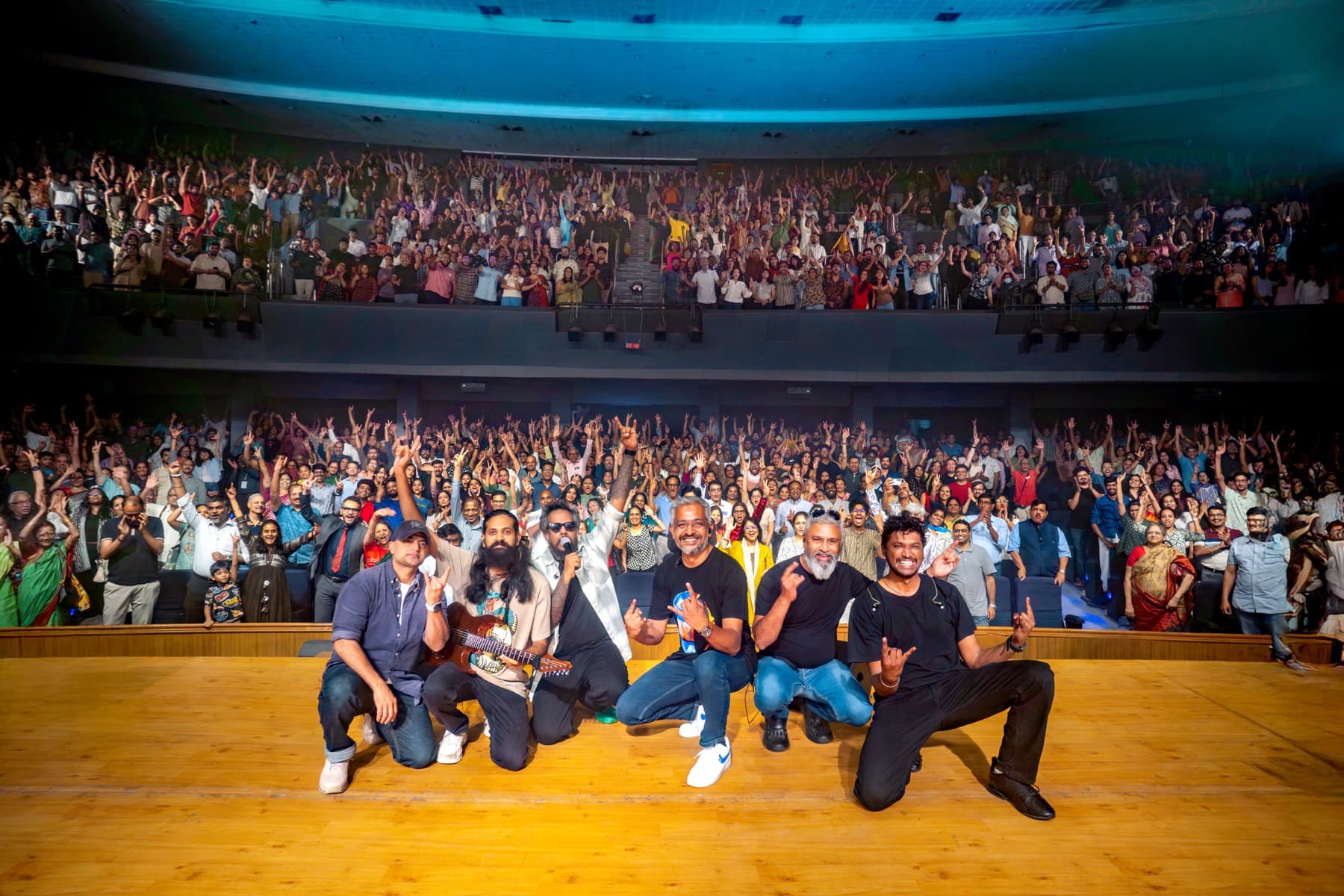 Agam posing on stage with a large cheering audience behind them