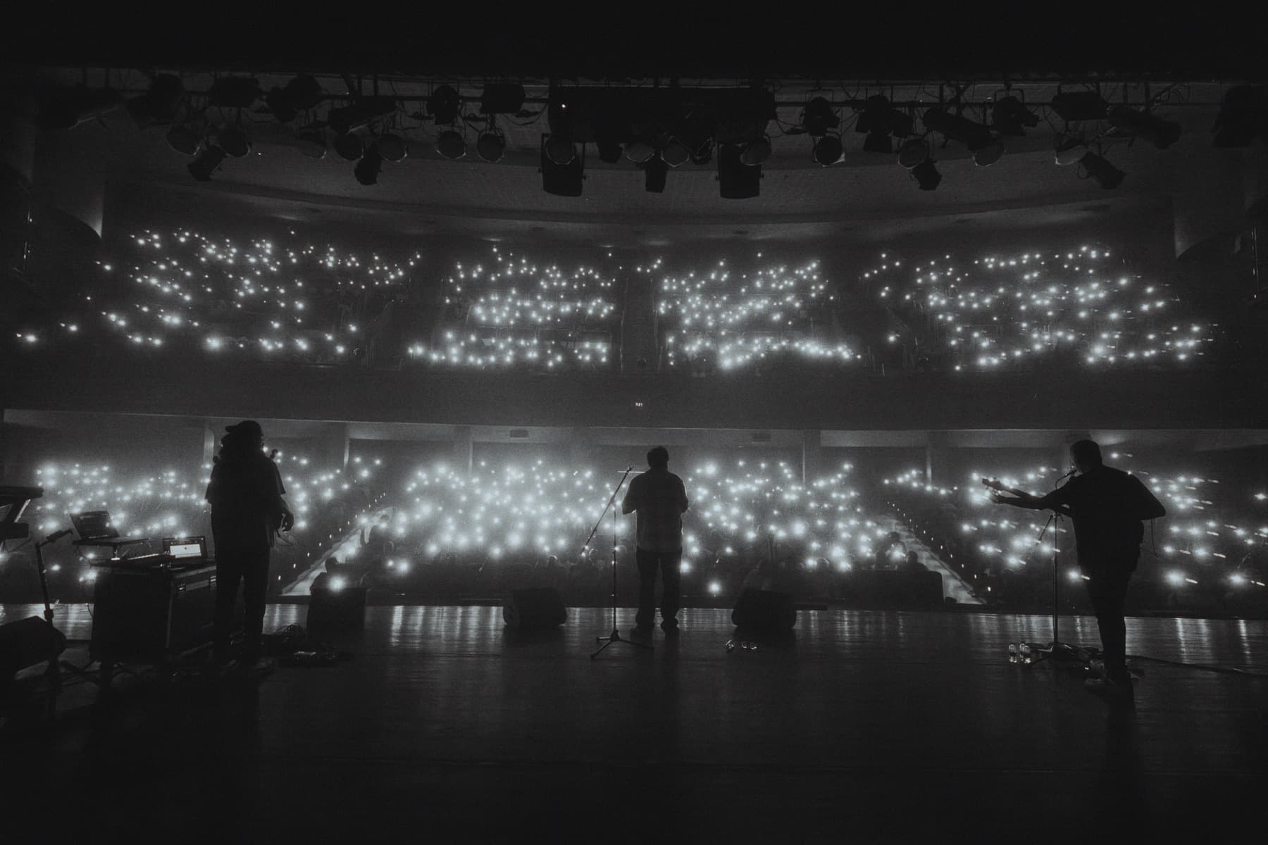 Agam silhouetted on stage before an audience holding phone lights